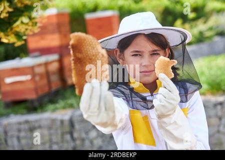 Porträt eines Mädchens, das im Sommer Honigwaben analysiert und Schutzanzug im Bienengarten trägt Stockfoto