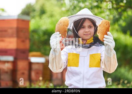 Ein Mädchen, das Bienenwachs untersucht und im Sommer Schutzanzug im Bienengarten trägt Stockfoto