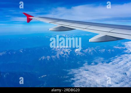 Neblige Berggipfel aus dem Flugzeug, das mit dem Flugzeugflügel über den alpen fliegt. Stockfoto