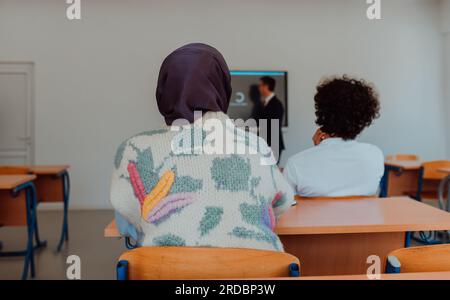 Eine vielfältige Gruppe von Schülern hört aufmerksam zu, nimmt aktiv Teil und begrüßt die moderne Bildung in einem dynamischen Klassenzimmer Stockfoto