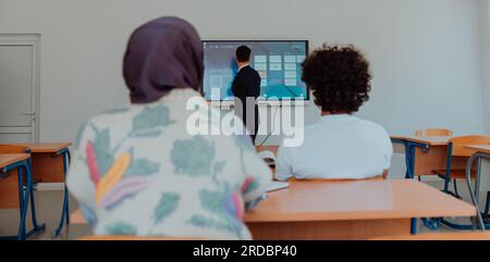 Eine vielfältige Gruppe von Schülern hört aufmerksam zu, nimmt aktiv Teil und begrüßt die moderne Bildung in einem dynamischen Klassenzimmer Stockfoto