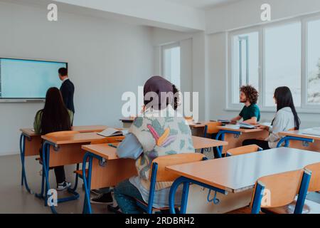 Eine vielfältige Gruppe von Schülern hört aufmerksam zu, nimmt aktiv Teil und begrüßt die moderne Bildung in einem dynamischen Klassenzimmer Stockfoto