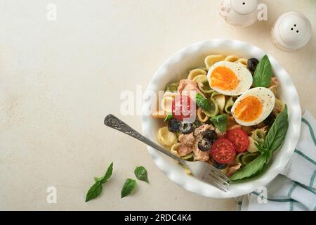 Italienischer Nudelsalat. Orekchiette-Pasta mit Thunfisch, Tomatenkirsche, Oliven, Basilikum und Parmesan auf grauem Stein- oder Betonhintergrund. Rz Stockfoto