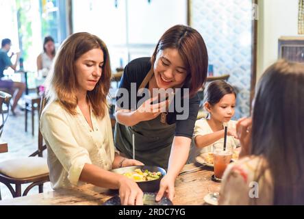 Vietnamesische Kellnerin putzt Tisch für Gäste im Café und zeigt vietnamesische Kultur und Höflichkeit Stockfoto