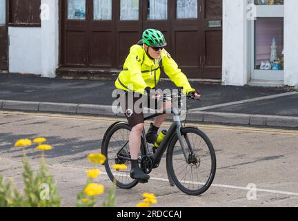 Seitenansicht eines männlichen Radfahrers mit Fahrradhelm und gut sichtbarem Oberteil, der auf einem Fahrrad entlang einer Straße in Großbritannien fährt. Ein Radfahrer mit Warnausrüstung. Stockfoto