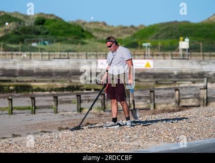 Mann am Kieselstrand mit Metalldetektor, der nach verlorenen oder wertvollen Gegenständen sucht, am Meer in Großbritannien. Metalldetektorin. Stockfoto