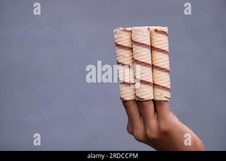 Handgehaltene Waferrollen mit Schokolade auf grauem Hintergrund, Nahaufnahme Stockfoto