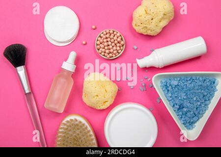 Generische Kosmetikprodukte Gläser Flaschen auf fuchsiafarbenem Hintergrund. Make-up-Pinsel, Wattepads, Cremebecher, Badesalz in der Schüssel, Meeresschwamm. Stockfoto