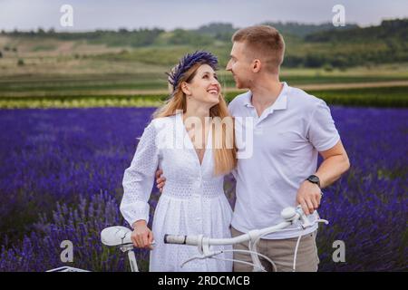 Das junge Paar steht auf einem Lavendelfeld in einer lächelnden Stimmung mit einem weißen Fahrrad Stockfoto