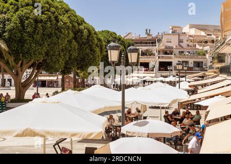 Die Menschen genießen es auf der Terrasse unter den Sonnenschirmen auf dem Platz des spanischen Bergdorfes Mijas in Andalusien in Spanien. Stockfoto