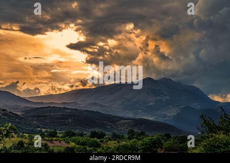 Landschaft des Gebirges Sirente-Velino unter einem stürmischen Himmel mit Wolken, die vom roten Licht des Sonnenuntergangs beleuchtet werden. Naturschutzgebiet Sirente Velino Stockfoto