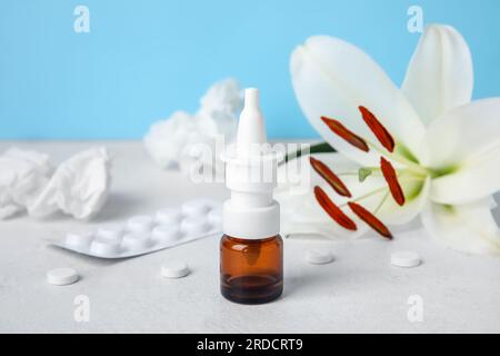 Nasentropfen mit Pillen, Blüten und Taschentüchern auf dem Tisch nahe der blauen Wand, Nahaufnahme. Saisonales Allergiekonzept Stockfoto