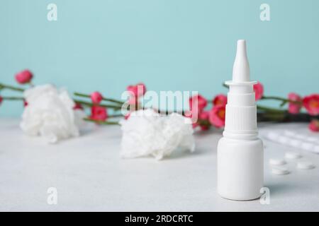 Nasentropfen mit Pillen, Blumen und Taschentüchern auf dem Tisch nahe der blauen Wand. Saisonales Allergiekonzept Stockfoto