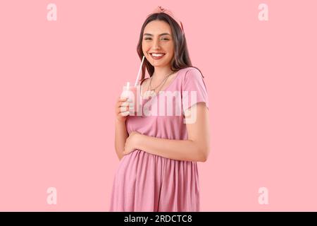 Junge schwangere Frau mit einem Glas Smoothie auf pinkfarbenem Hintergrund Stockfoto