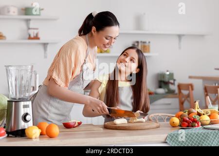 Ein kleines Mädchen mit ihrer Mutter schneidet Bananen für Smoothie in der Küche Stockfoto