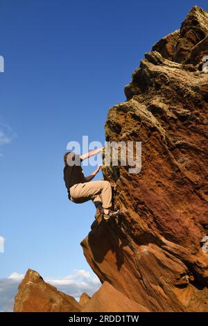 Ein junger Mann, der auf Agglestone Rock klettert. Stockfoto