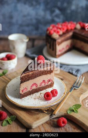 Schokoladen-Himbeerkuchen mit Schokoladen-Ganache und frischen Himbeeren auf der Oberseite. Schneidbrett aus Holz. Blauer Hintergrund. Stockfoto