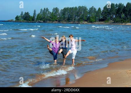 Drei Schwestern kehren in ihre Kindheit zurück und treten und planschen im Wasser des Lake Superior auf der Oberen Halbinsel, Michigan. Sie lachen und treten Stockfoto