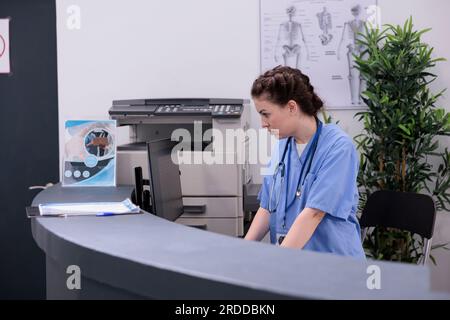 Assistentin an der Rezeption, die medizinische Expertise am Computer prüft, während sie Patienten-Check-up-Besuche plant. Medizinische Fachkräfte sind in der Diagnose und Behandlung verschiedener Krankheiten geschult. Stockfoto