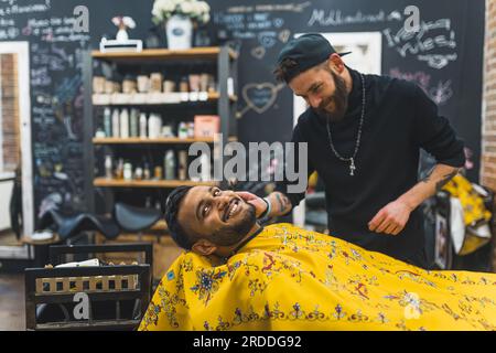 Ein lächelnder indischer Klient, der sich von einem Friseur den Bart schneiden lässt. Lächelnd. Hochwertiges Foto Stockfoto