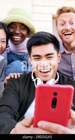 Gruppe lächelnder Menschen, die im Freien ein Mobiltelefon benutzen. Fröhliche Jungs und Mädchen Freunde, die Spaß haben, etwas am digitalen Display zu sehen. Frohe Ferien Stockfoto