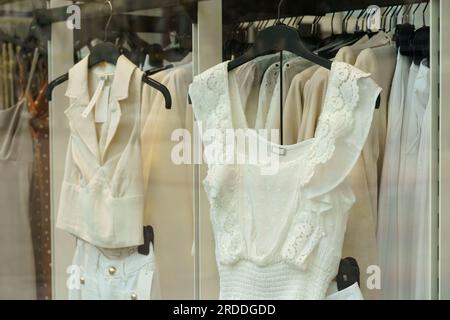 Helle Damenbekleidung hängt hinter Glas in einem Schaufenster auf Ausstellungsregalen. Stockfoto
