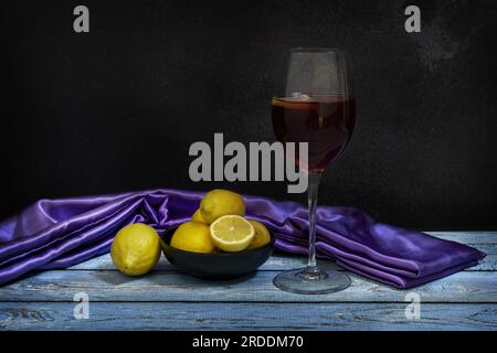 Ein Glas Sangria mit Rotwein und Zitrone in einer schwarzen Schüssel mit Zitronen auf einem blauen Tisch Stockfoto