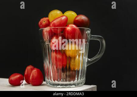 Ein kleines klares Glasgefäß gefüllt mit reifen Kirschtomaten verschiedener Sorten Stockfoto