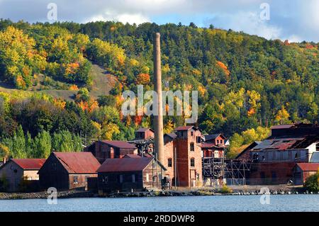 Gebäude und Rauchschichten des historischen Quincy Copper Smelter auf der Oberen Halbinsel Michigan sind geschlossen und ungenutzt. Quincy Hill im Hintergrund zeigt Fal Stockfoto