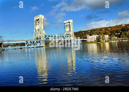 Das ruhige Wasser des Portage Lake spiegelt das Bild der Portage Lift Bridge wider, die Houghton und Hancock, Michigan, verbindet. Die Farben des Herbstes decken Quincy Hill i ab Stockfoto