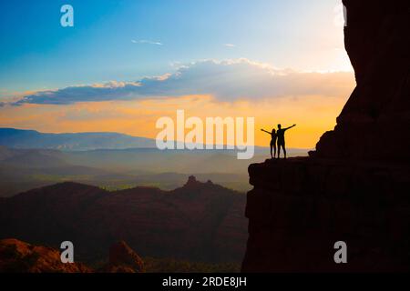 Silhouette von Vater und Tochter auf dem Weg am Cathedral Rock bei Sonnenuntergang in Sedona. Der farbenfrohe Sonnenuntergang über Sedonas Cathedral Rock Wahrzeichen. Stockfoto