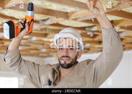 bauer mit Akku-Bohrer an Holzdecke über Kopf Stockfoto