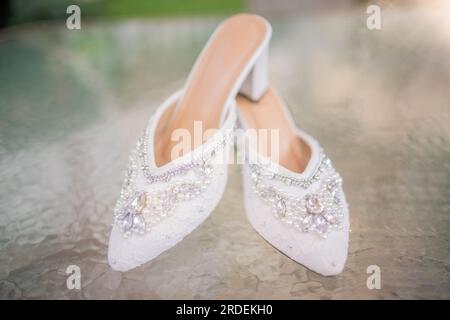 Hochzeitsschuhe mit spitzen Zehen. Schuhe mit hohen Absätzen. Frauenfüße in luxuriösen Sommerschuhen für Damen. Elegante Hausschuhe für Damen auf dem Boden. Fash Stockfoto