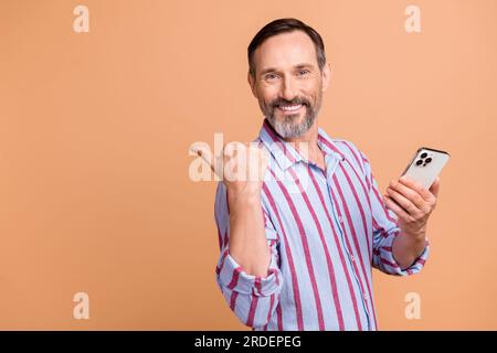 Foto eines älteren Mannes, der auf leeren Raum hinweist facebook twitter Telegramm instagram hält Smartphone isoliert auf beigefarbenem Hintergrund Stockfoto