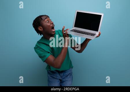 Überraschend fröhlicher afrikanischer junger brünetter männlicher Berater in lässigem T-Shirt mit offenem Laptop Stockfoto