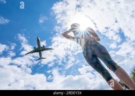 Ein schönes blondes Modell genießt einen Sommertag, während ein kommerzielles Flugzeug über dem Himmel fliegt Stockfoto