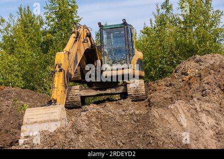 Der gelbe Hydraulikbagger arbeitet an einem Sommertag auf einem Haufen Erde Stockfoto