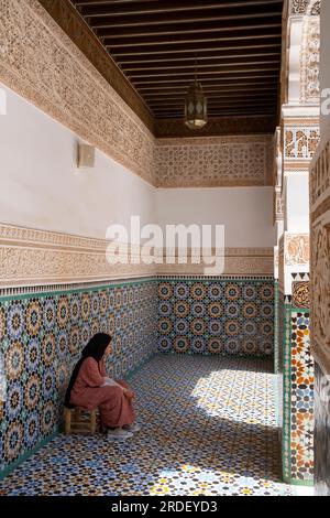 Marokko: Eine Frau, die in einer der Galerien um den zentralen Innenhof sitzt, Ben Youssef Madrasa (Medersa Ben Youssef), Medina von Marrakesch, Marrakesch. Der Sultan der Saadier-Dynastie, Abdallah al-Ghalib Billah (1517 - 1574), baute die Madrasa im Jahr 1565 (972 AH). Es war einst das größte islamische College im Maghreb (Nordwestafrika). Stockfoto