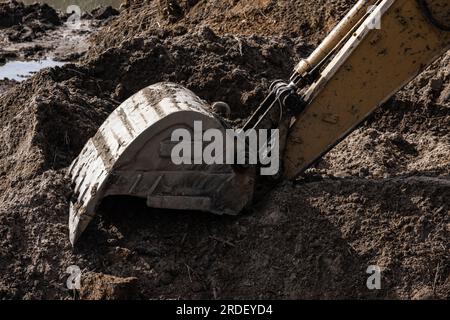 Die schmutzige Schaufel des Hydraulikbaggers befindet sich an einem Sommertag auf einem Haufen dunklen Bodens Stockfoto