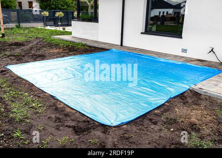 Rollender gelber Sand mit einer Stahlrolle für einen Gartenpool, sichtbare blaue Plane. Stockfoto