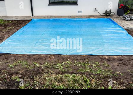Rollender gelber Sand mit einer Stahlrolle für einen Gartenpool, sichtbare blaue Plane. Stockfoto