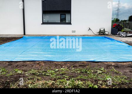 Rollender gelber Sand mit einer Stahlrolle für einen Gartenpool, sichtbare blaue Plane. Stockfoto