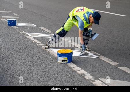 Ein Straßenarbeiter bringt Markierungen an, die den Radweg von der Straße für Autos in der Stadt trennen. Stockfoto