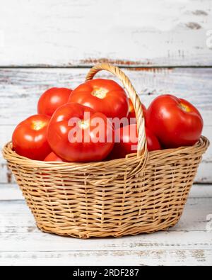 Frische rohe Tomaten in einem Korb auf Holzhintergrund. Tomatenerntezeitkonzept. Gemüse für eine gesunde Ernährung Stockfoto
