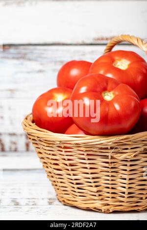 Frische rohe Tomaten in einem Korb auf Holzhintergrund. Tomatenerntezeitkonzept. Gemüse für eine gesunde Ernährung. Schließen Stockfoto