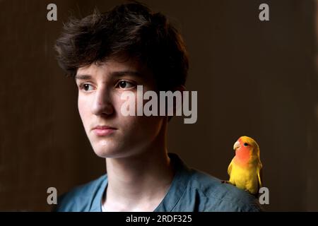 14-jähriger Junge mit einem Liebesvogel auf der Schulter. Stockfoto