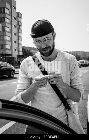 Ein junger, stilvoller Mann, der eine Zigarette auf der Straße rollt. Stockfoto