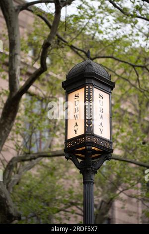 Eine NYC U-Bahn-Lampe vor einem Steingebäude mit Ästen Stockfoto