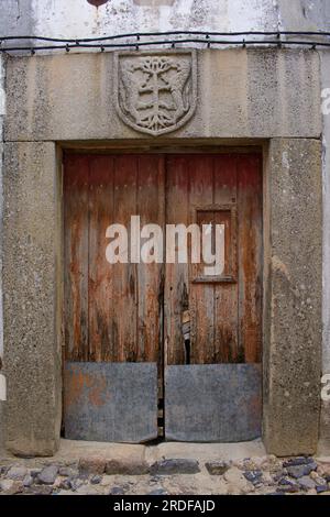 Castelo de Vide, Portugal. Massiver steingerahmter Eingang zum Haus in der Altstadt - alte Holztür, Wappen in Steinlintel geschnitzt. Stockfoto