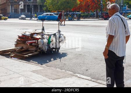 Havanna, Kuba - 27. Mai 2023: Ein Mann schaut auf einen rustikalen Wagen in einer Stadtstraße. Der selbstgemachte Karton wird zum Sammeln von Pappe verwendet, die an Regierungsbeamte verkauft wird Stockfoto